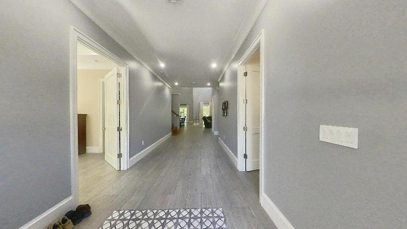 The 2024 entry hall, looking through the main artery of the residence with wide-plank floors, full-height casework, and recessed lighting